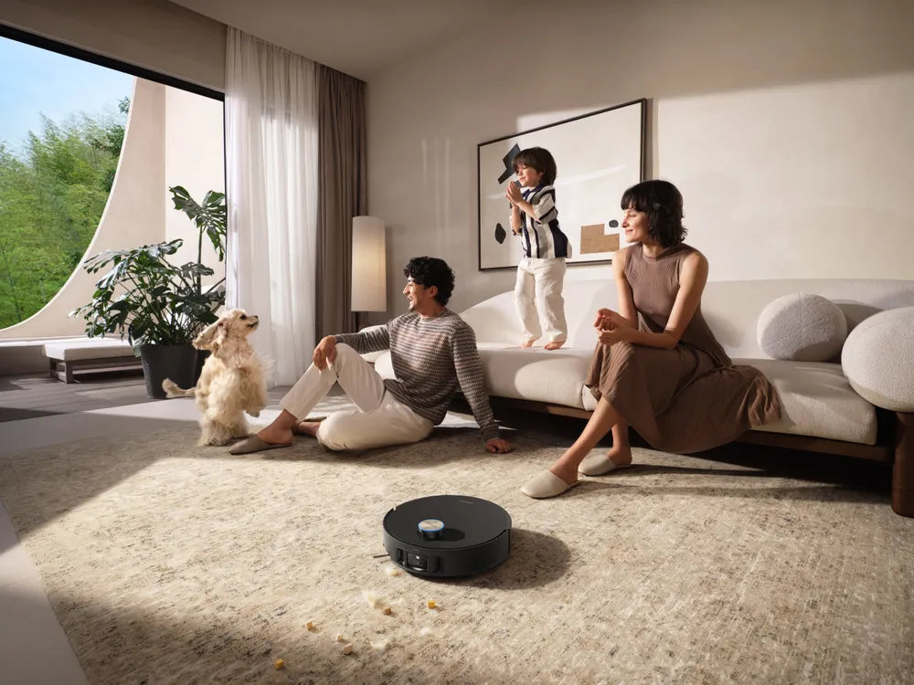 Dreame robot vacuum cleaning a rug scattered with crumbs while a family and their dog look on.
