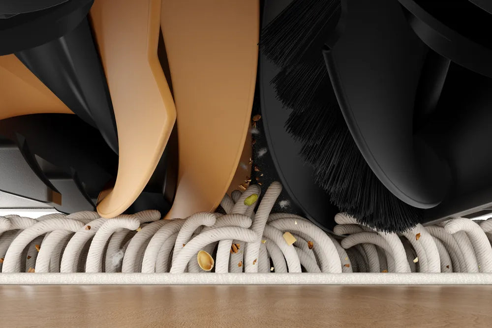 Close-up of a Dreame robot vacuum's dual roller brush lifting crumbs and debris from a looped rug.