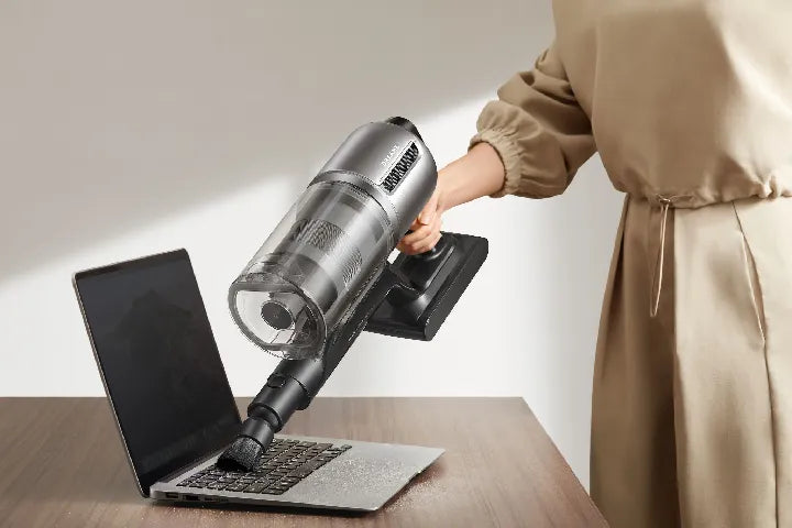 Rotating soft dusting brush lifting crumbs off a laptop surface.