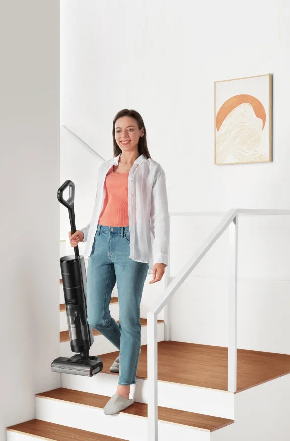 Woman carrying a Dreame Wet Dry Vacuum down the stairs in a bright home.