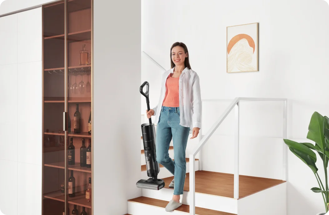 Woman carrying a Dreame Wet Dry Vacuum down the stairs in a bright home.